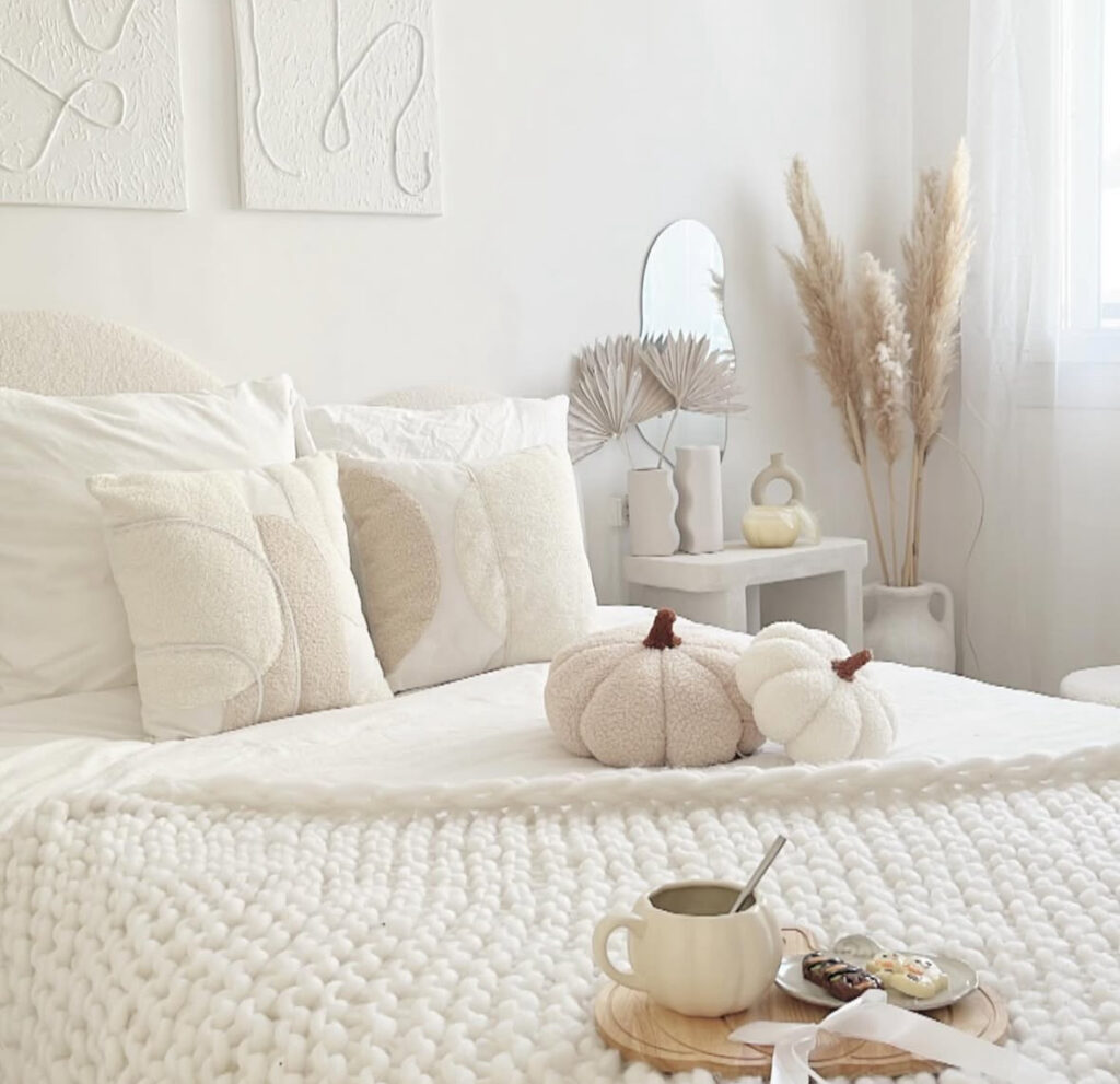 All-white minimalist bedroom with boucle pumpkins, chunky knit throw, pampas grass and soft textures — simple fall bedroom decor ideas.