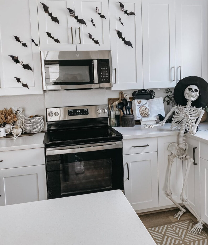 White kitchen cabinets with peel-and-stick bats and a poseable skeleton in a witch hat by the counter.