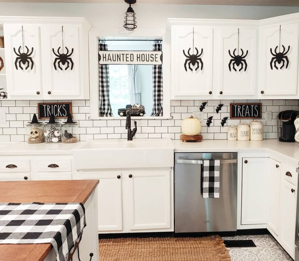 Removable paper spiders on white cabinets with gingham curtains and a “Haunted House” sign by the window.