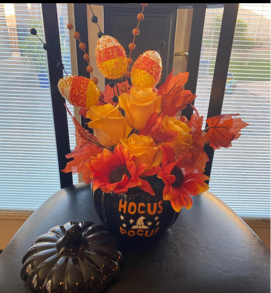 Black cauldron filled with orange and yellow flowers and candy-corn picks, arranged as a cheerful Halloween centerpiece