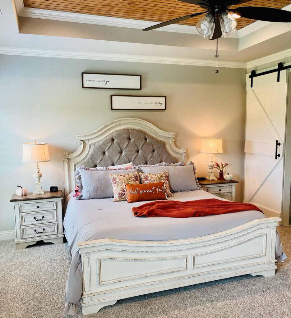 Traditional master bedroom with tufted bed, rust throw blanket, seasonal pillows, barn door and warm lamps — fall master bedroom ideas.