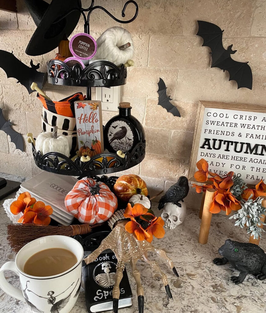 Tiered coffee bar tray with pods, mini pumpkins, a tiny cauldron, and wall bats overhead.