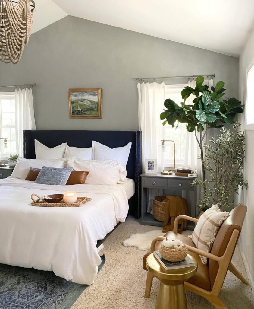 Calm fall bedroom with navy headboard, leather pillows, candle tray, fiddle-leaf fig and gold side table pumpkins — cozy fall bedroom decor ideas.