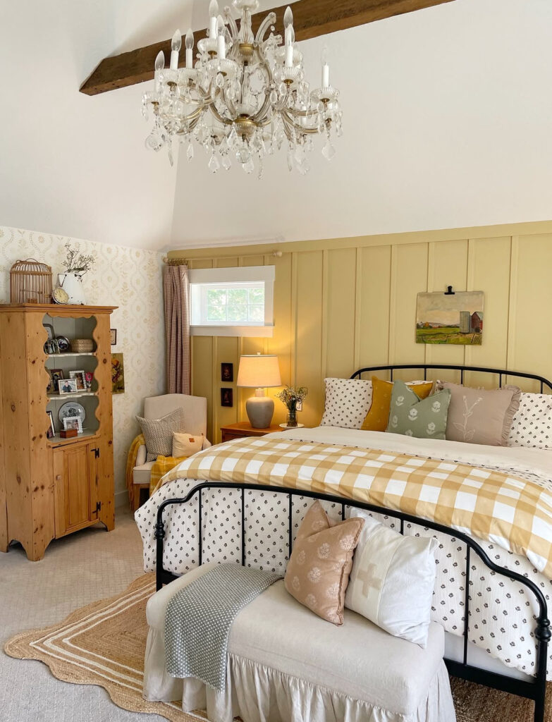 Charming cottage room with chandelier, yellow board-and-batten, gingham duvet and bench pillows — cottage fall bedroom decor ideas.