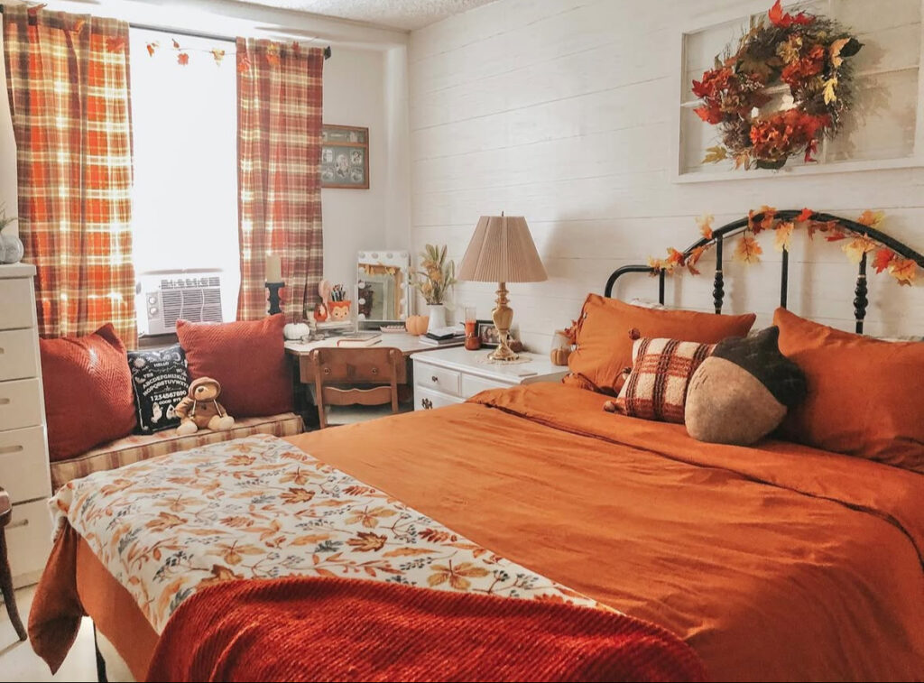 Cottage fall bedroom with plaid curtains, orange bedding, leaf wreath and plaid accent pillow — fall decor ideas for bedroom.