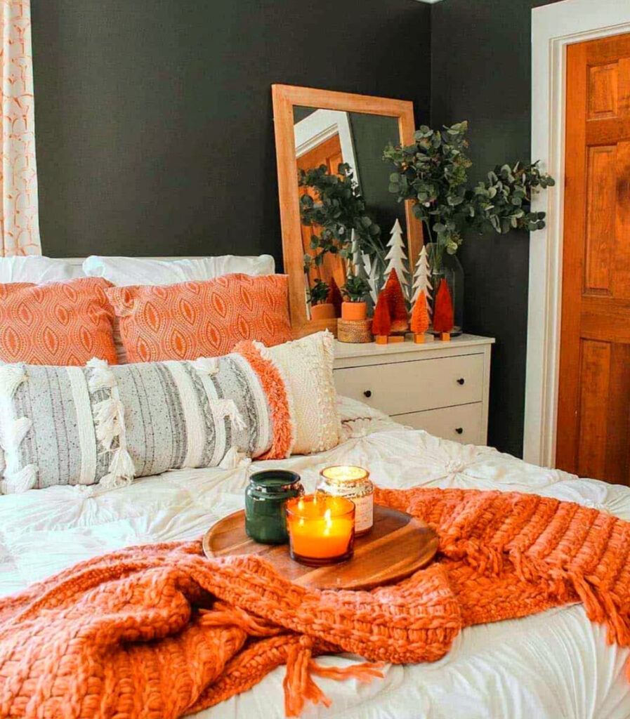 Moody fall bedroom with dark accent wall, orange knit throw, candles and textured pillows — cozy fall bedroom ideas.