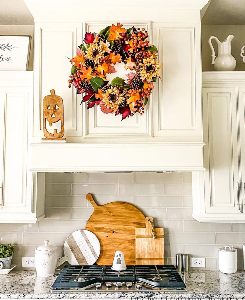 Fall floral wreath above a range hood with stacked cutting boards and a tiny ceramic ghost.