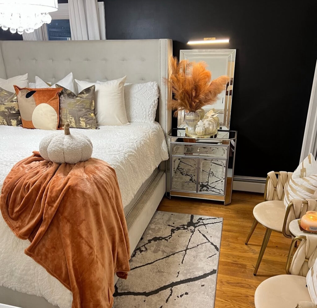 Glam bedroom with black accent wall, mirrored nightstand, pampas, rust throw and plush pumpkin — glam fall bedroom decor ideas.