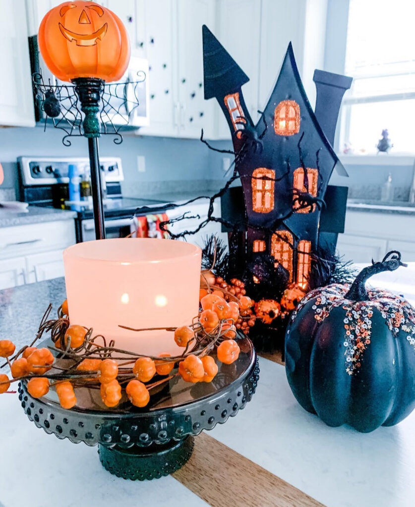 Candlelit Halloween vignette with black pumpkin, orange berry garland, and mini haunted house on the kitchen counter.