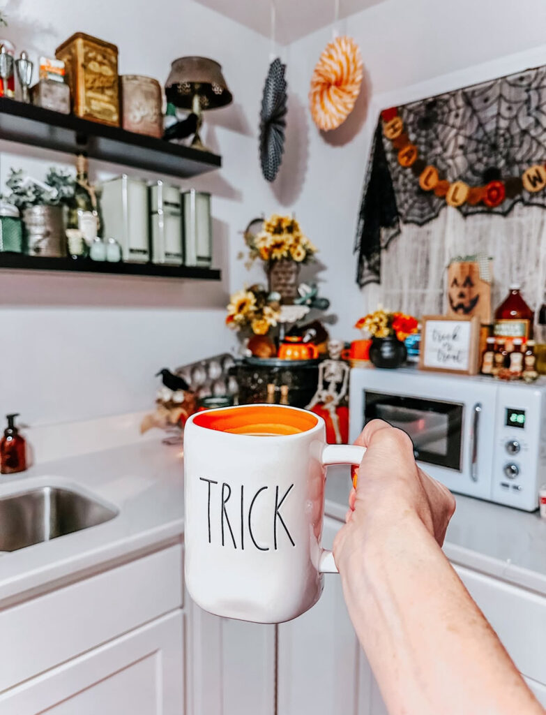 Playful coffee nook with Halloween mug, small banner, and festive paper fans on a kitchen counter.