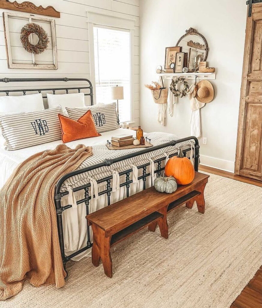 Shiplap farmhouse bedroom with iron bed, striped bedding, rustic bench pumpkins and vintage wall hooks — farmhouse fall bedroom ideas.