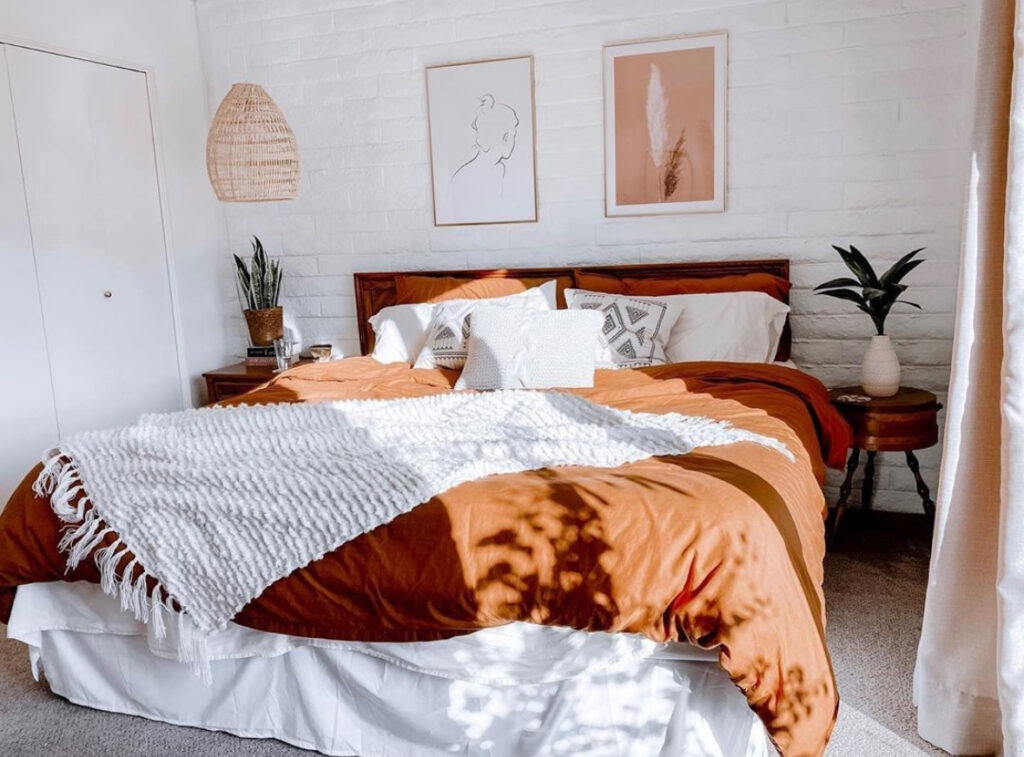 Minimal modern bedroom with rust duvet, chunky white knit blanket, pampas and neutral art — aesthetic fall bedroom ideas.