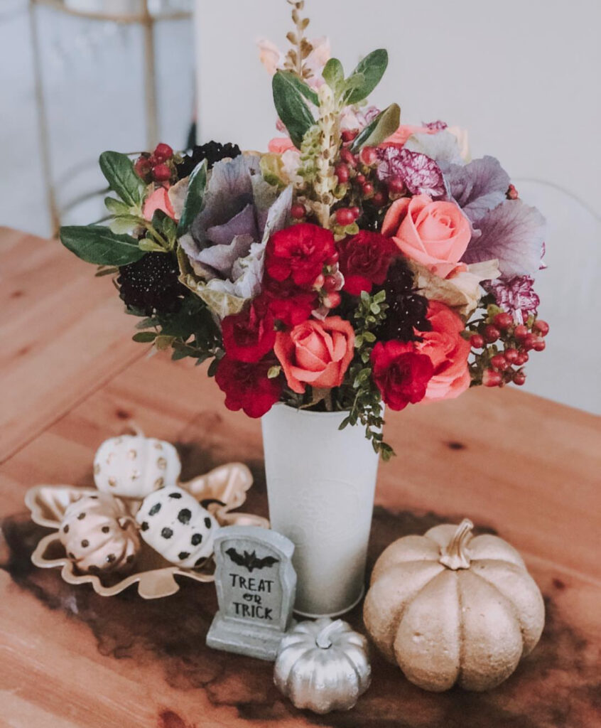 Moody fall arrangement with peach roses, burgundy berries, decorative cabbage leaves, and metallic mini pumpkins