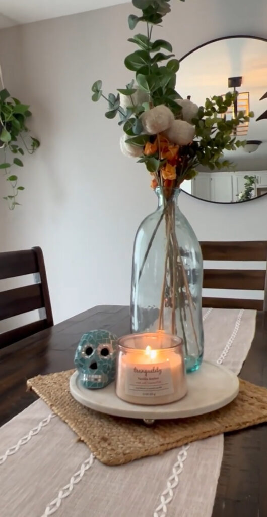 Minimal vignette featuring a clear bottle with eucalyptus, a pillar candle, and a small turquoise skull.
