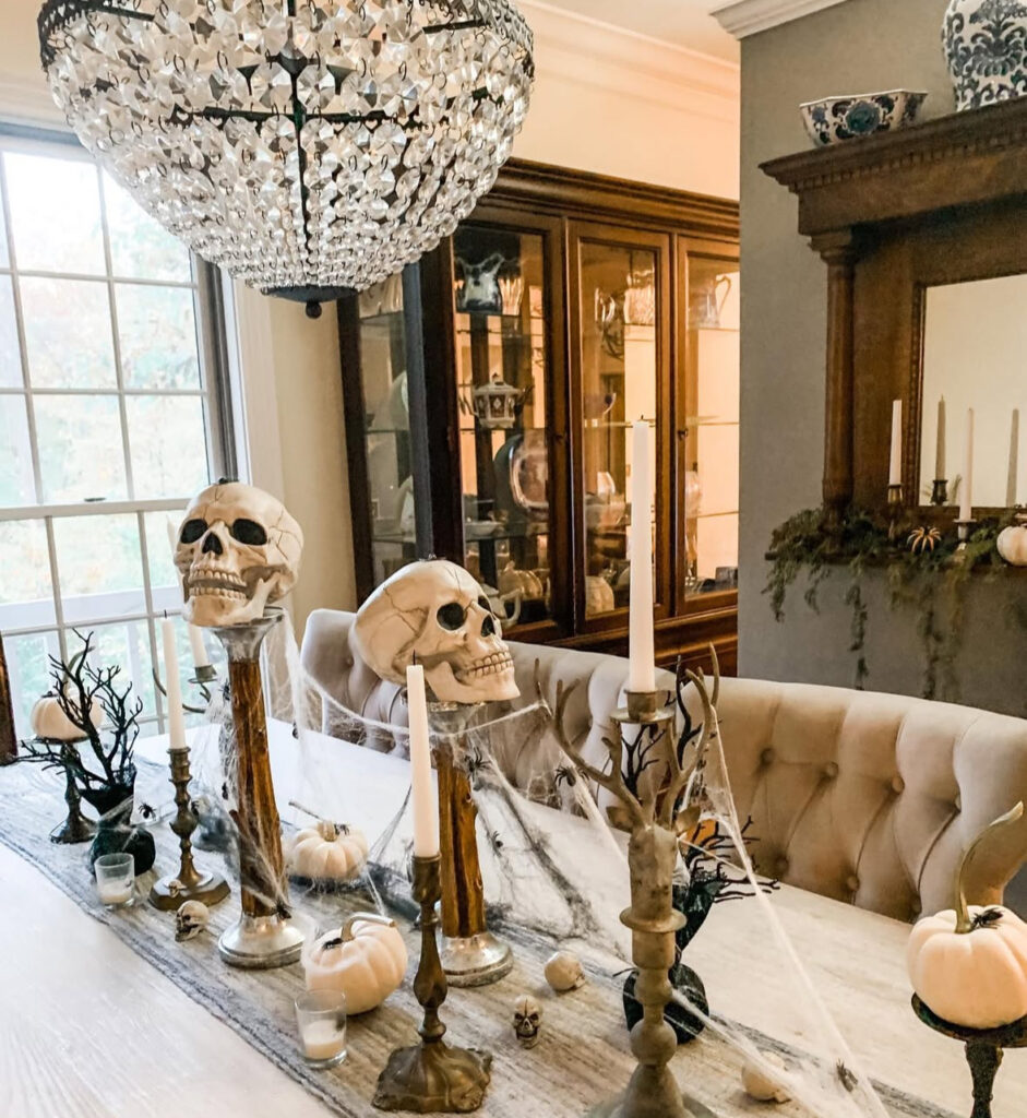 White skulls on candle pedestals with black taper candles and a cobweb runner along the table.