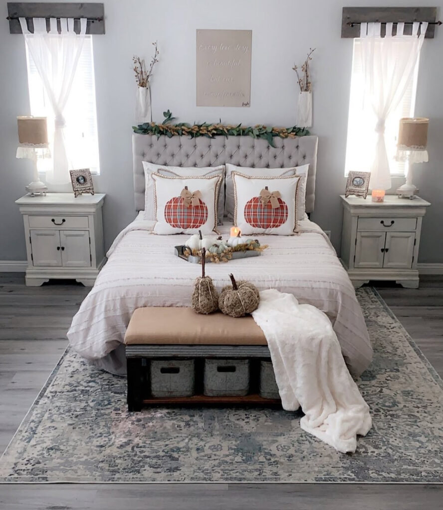 Farmhouse fall bedroom decor with tufted headboard, plaid pumpkin pillows, garland, candles, and bench pumpkins — fall bedroom decor ideas.