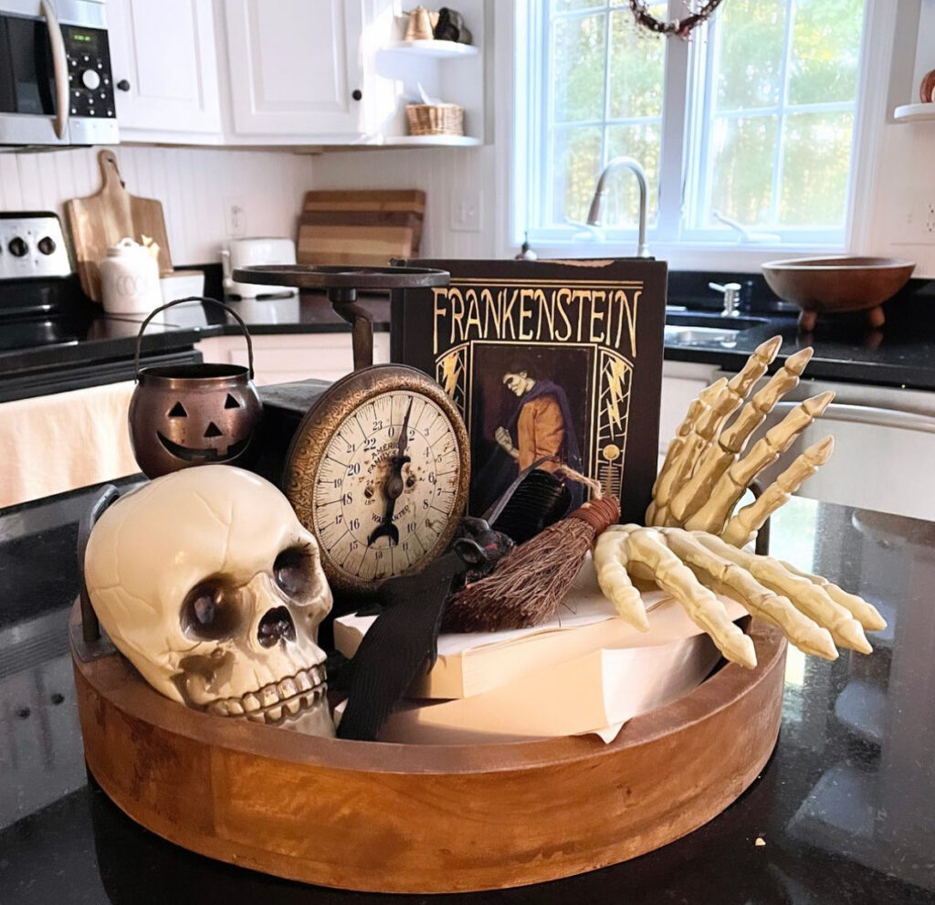 Vintage-style round tray filled with a skull, old scale, tiny broom, spooky book, and skeletal hand.
