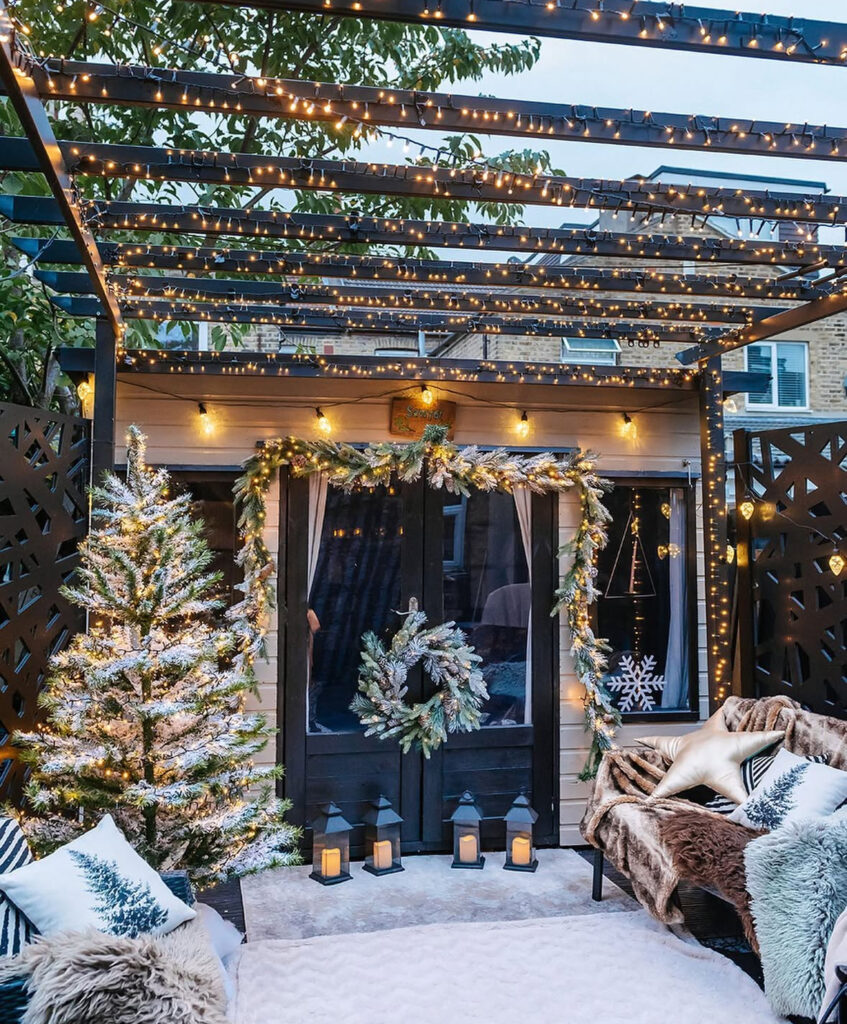 Pergola canopy of string lights with frosted garland, lanterns, and slim lit tree.