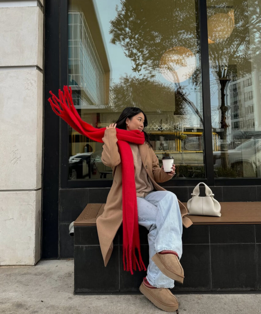 Camel coat with bright red scarf, light denim, and platform boots; takeaway coffee on the go.