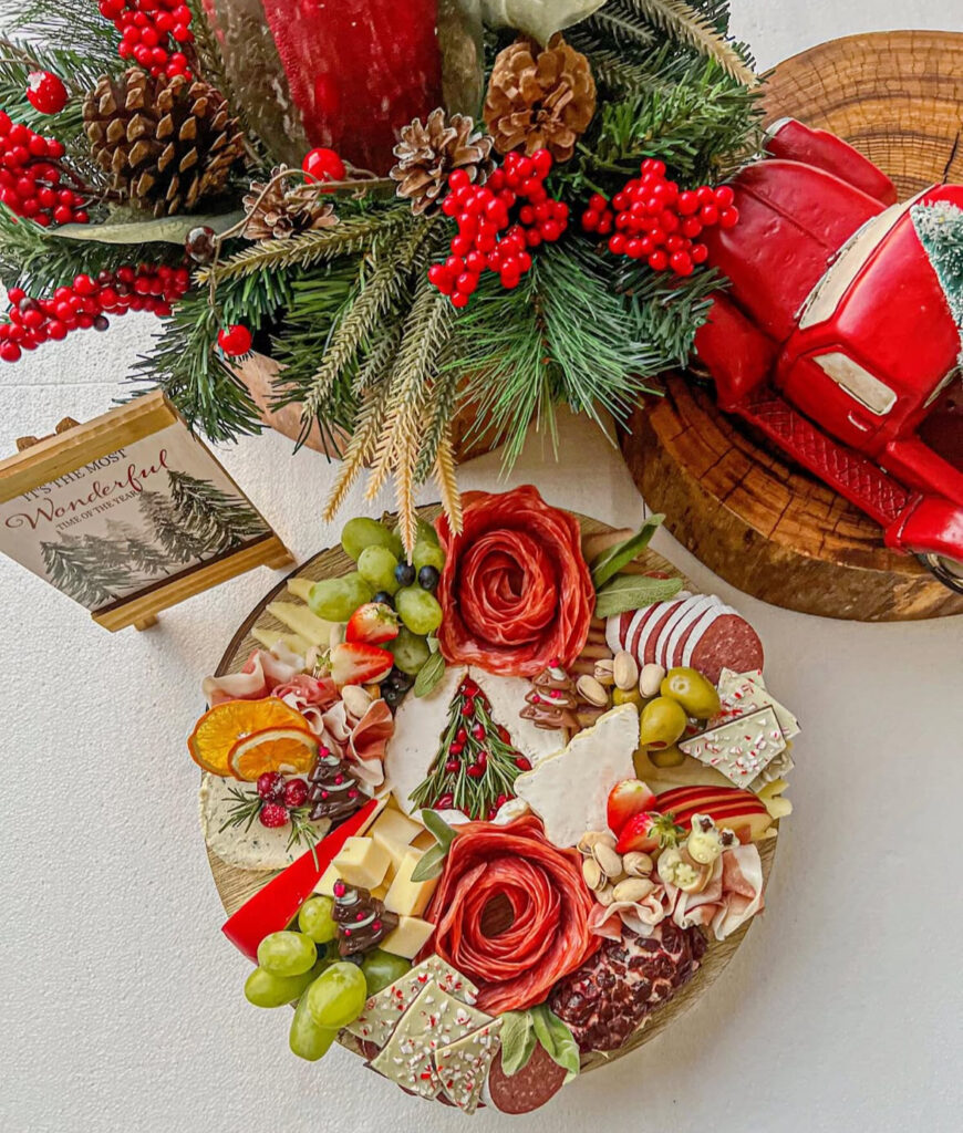 Festive board with salami rosettes, cheeses, fruit, olives, nuts, and a rosemary herb “tree” centerpiece.