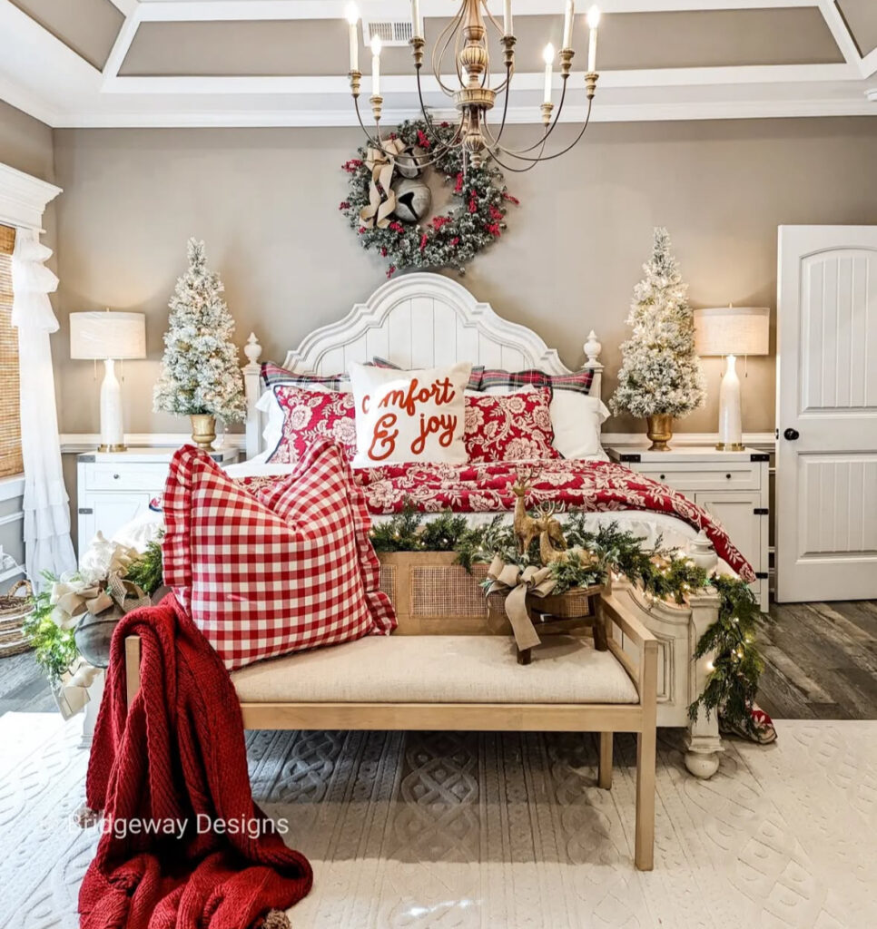 Two frosted trees, wreath, and layered pillows—elevated bedroom Christmas decor ideas for a traditional suite. Bench garland twinkles softly.