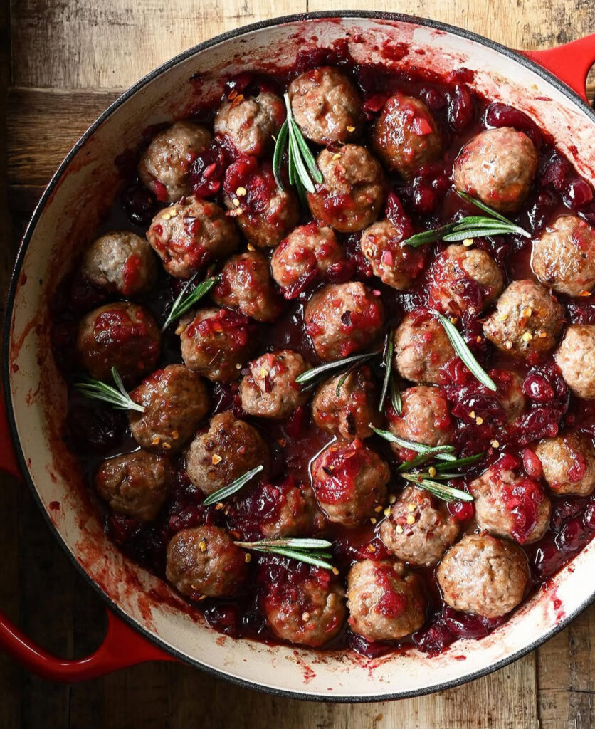 Skillet of glazed meatballs coated in glossy cranberry sauce with rosemary sprigs.