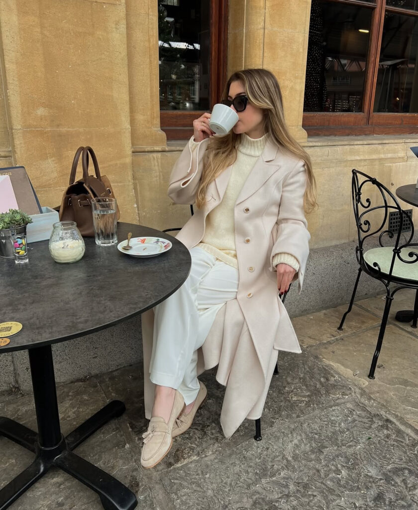 Ivory knit and milk-white coat with soft trousers and loafers inside a café.