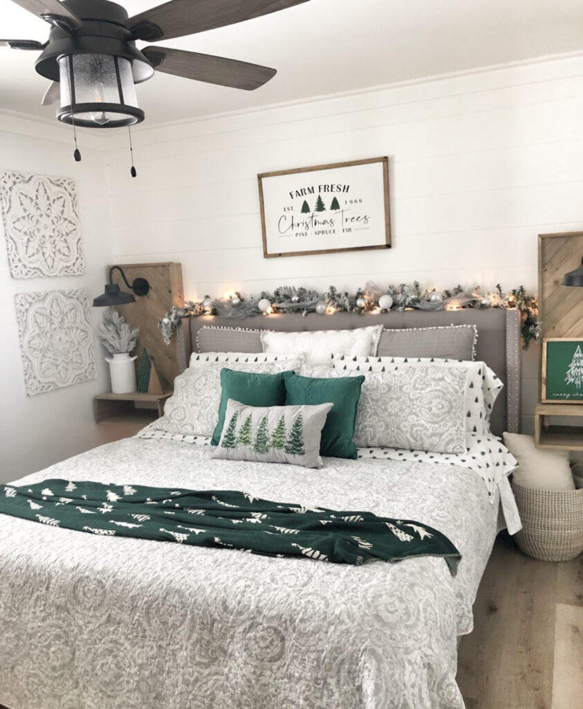 Soft gray-and-white room with evergreen garland and crisp linens—classic bedroom Christmas decor ideas without clutter. A small tabletop tree adds sparkle.