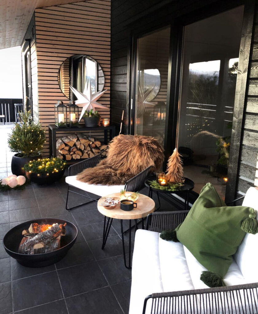 Cozy balcony with fire bowl, fur throw, twinkle lights, and mini evergreens.