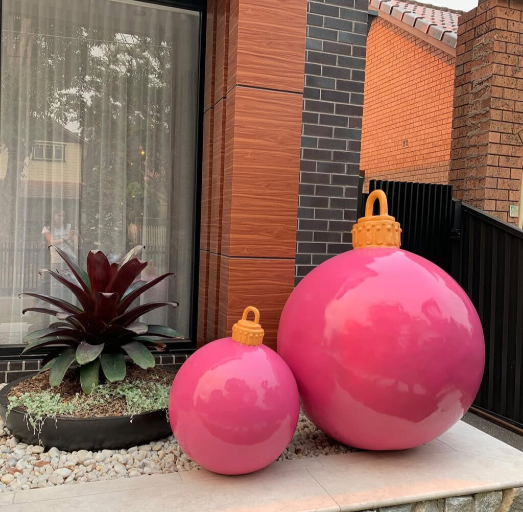 Oversized pink ornament sculptures by a modern entry with plants and stone.