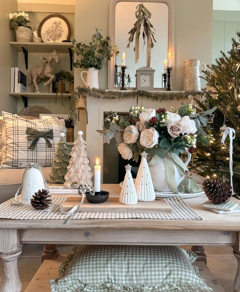 Cottage-style setup with gingham runner, floral arrangement, mini trees, pinecones, and taper candles; soft green room beyond.