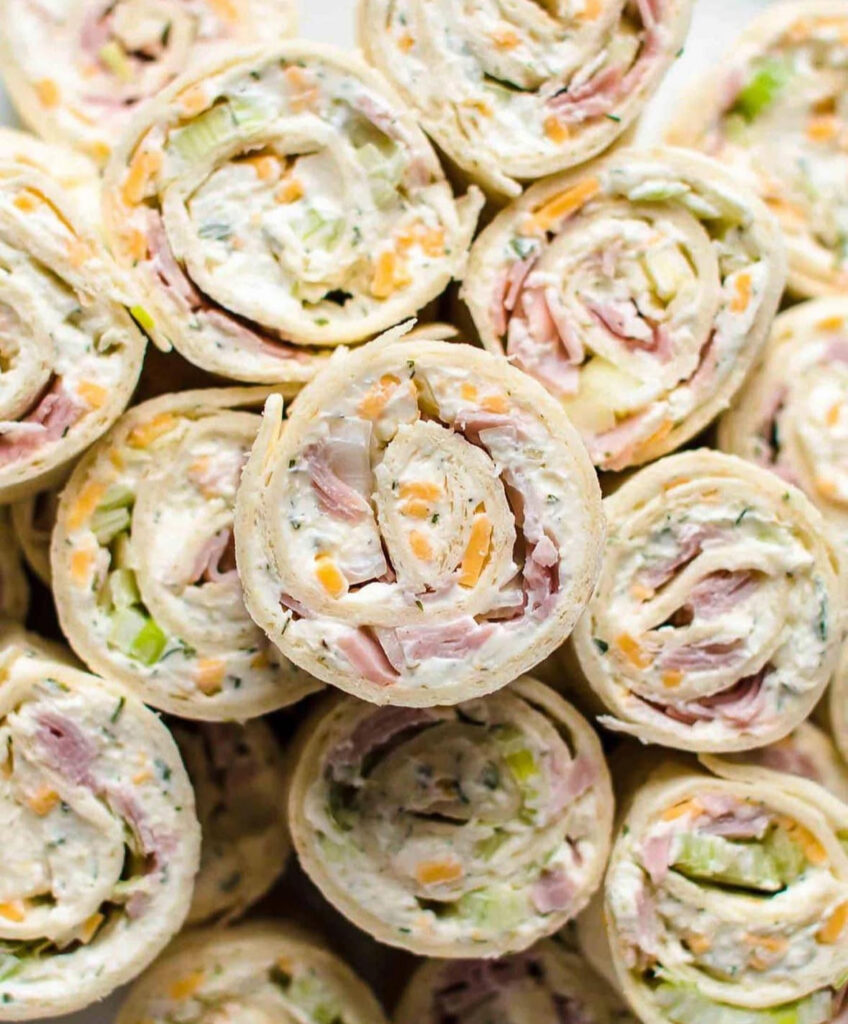 Close-up of tortilla pinwheels filled with ranchy cream cheese, diced ham, cheddar, and green onions, sliced into spirals on a platter.