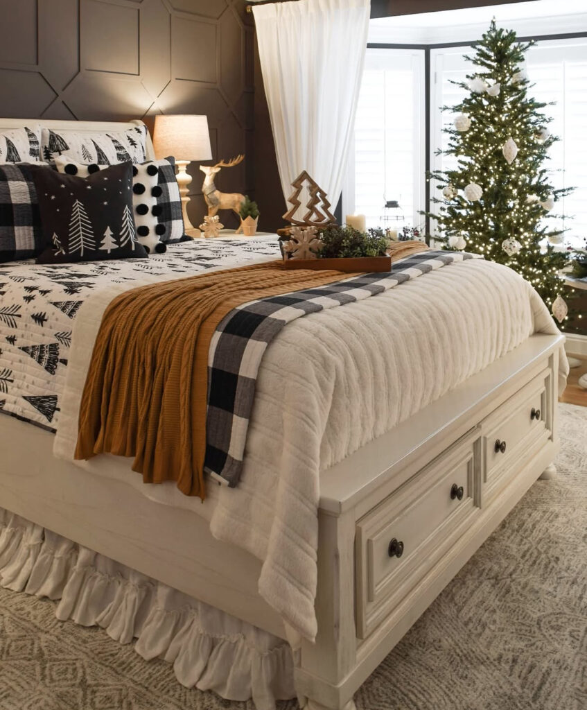Dark feature wall with white bedding, caramel throw, and lit tree—moody Christmas lights in bedroom ideas. Wood accents feel cabin-chic.