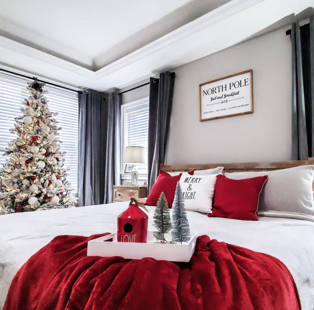 Sleek room with gray curtains, flocked tree, and tray decor—simple Christmas bedroom decor ideas in red and white. “North Pole” sign nods to the season.