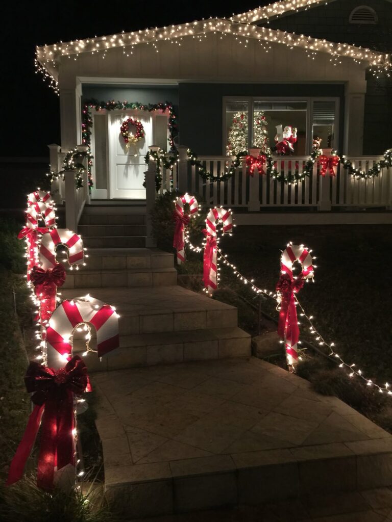 Walkway lined with lighted candy-cane stakes, garland railing, and roof icicle lights.