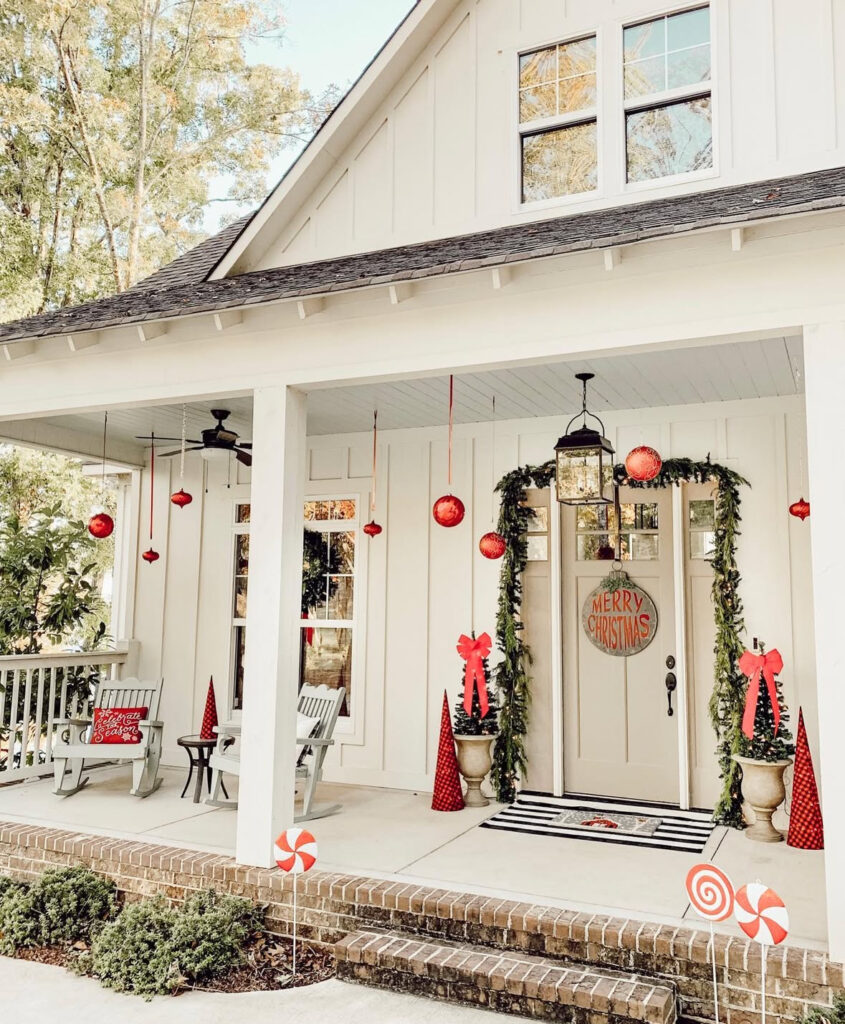 White porch with hanging red ornaments, candy accents, and striped doormat.