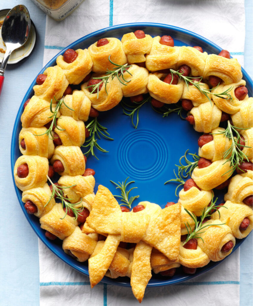 Festive board with salami rosettes, cheeses, fruit, olives, nuts, and a rosemary herb “tree” centerpiece.