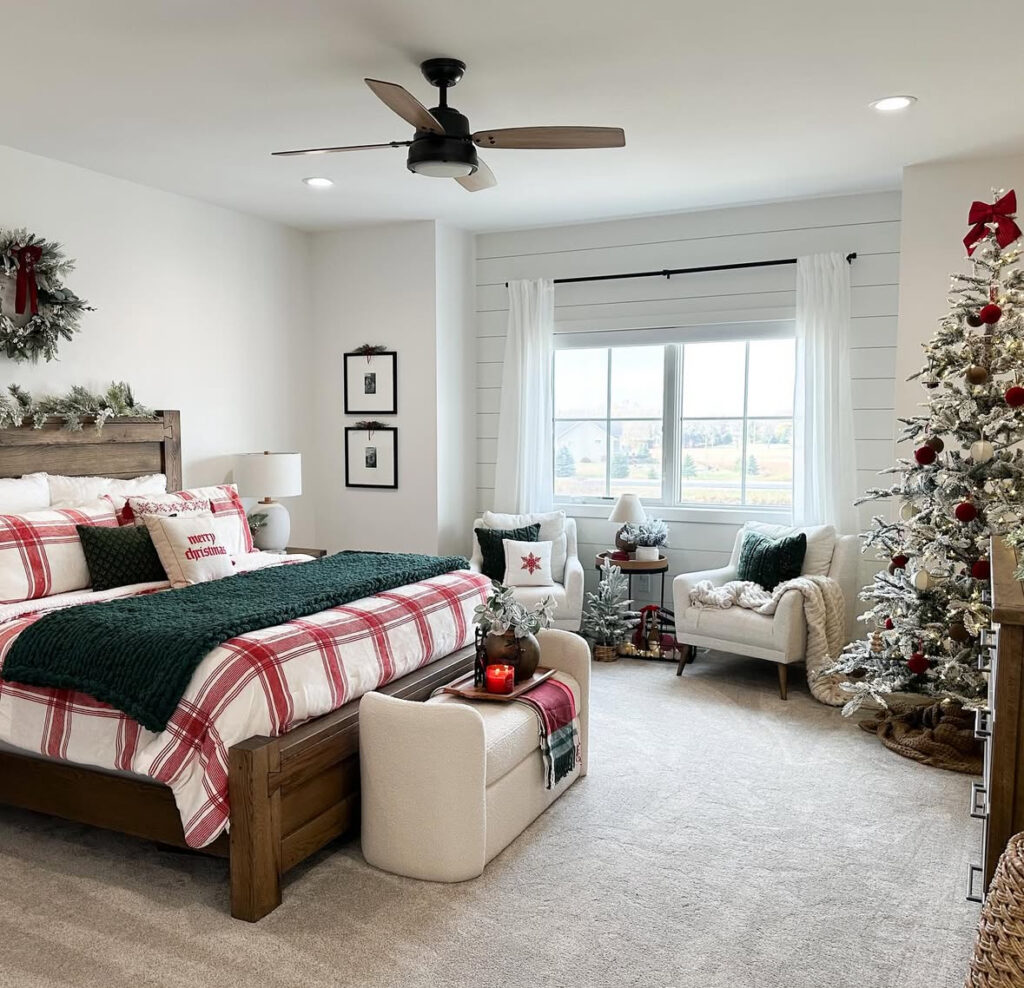 Spacious suite with plaid duvet, green knit, and seating area—livable bedroom Christmas decor ideas. Flocked tree and candles set the mood.