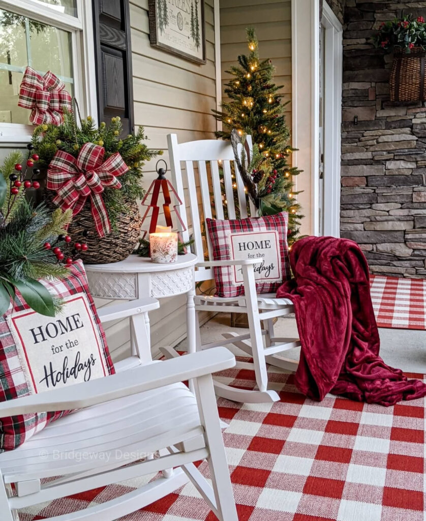 Farmhouse porch with plaid rug, rocking chairs, lanterns, and mini lit tree.