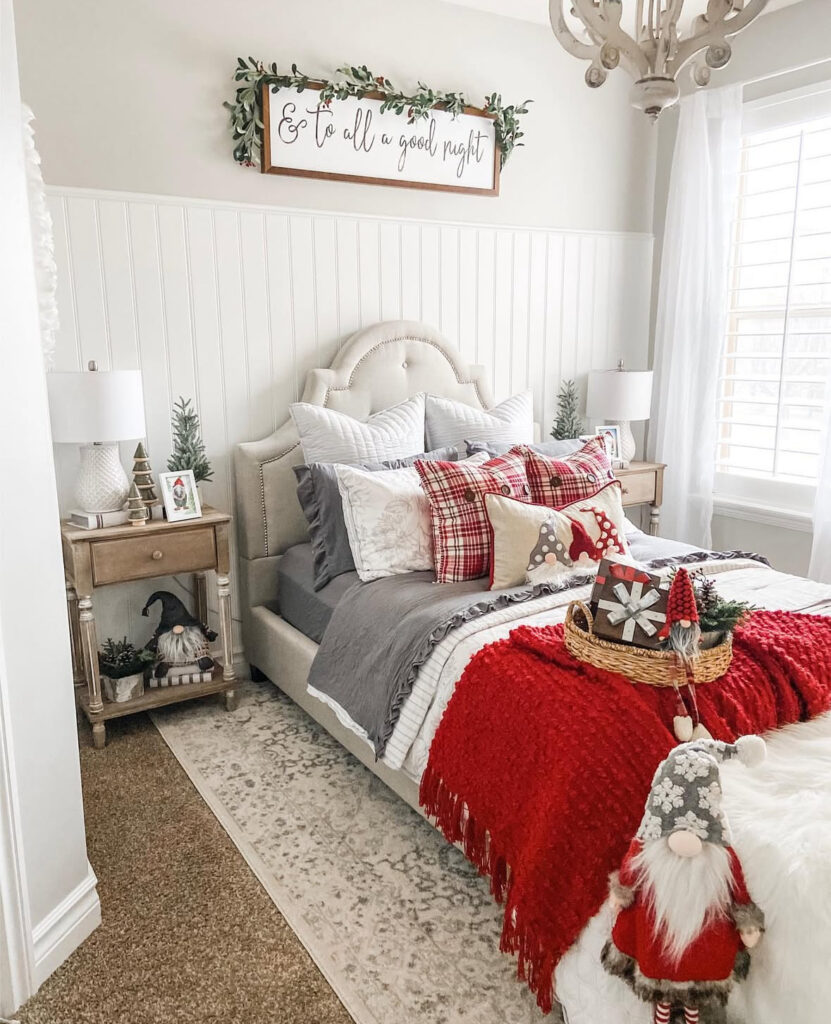 Neutral primary bedroom layered with plaid pillows and a red throw—cozy Christmas bedroom ideas for adults. Benches and bedside gnomes add whimsical charm.