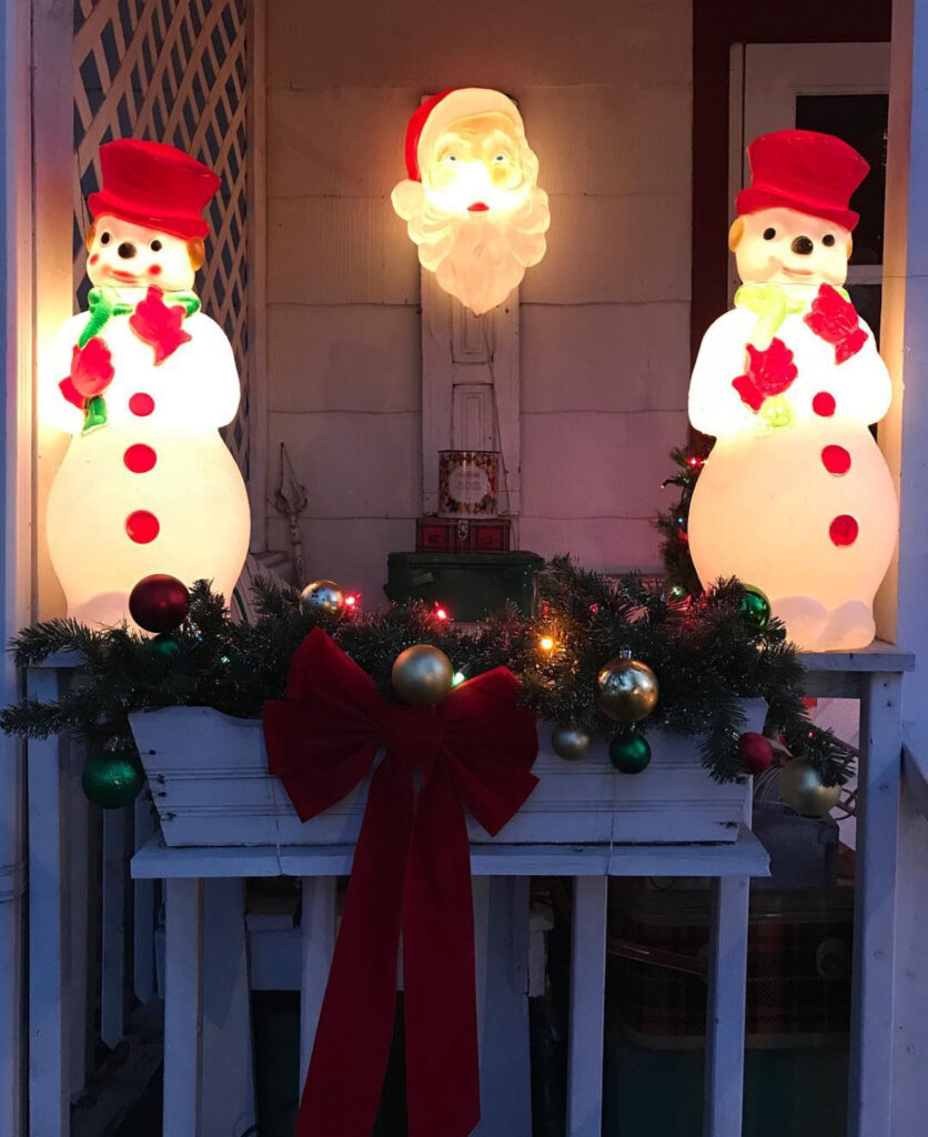 Retro blow-mold snowmen and Santa with garland, ornaments, and a big red bow.