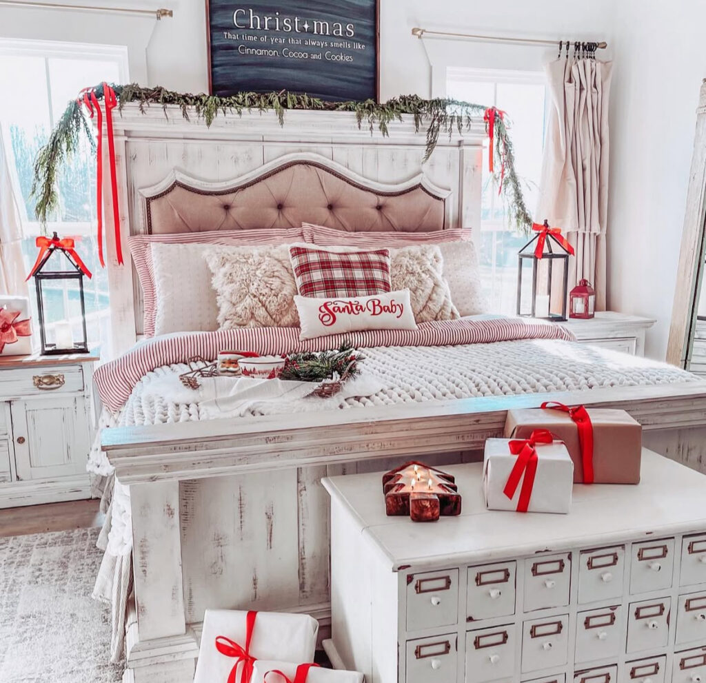 Whitewashed headboard with red bows, chunky knit, and gifts—romantic Christmas decoration ideas for bedroom. “Santa Baby” pillow adds a playful wink.