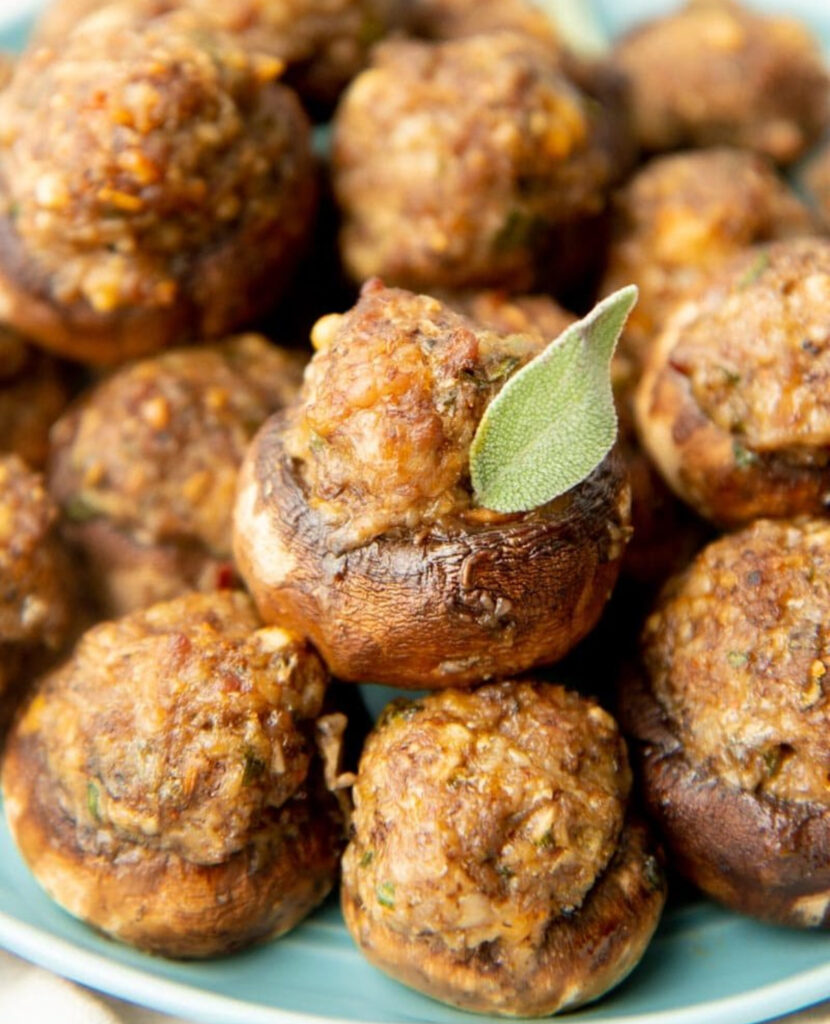 Close-up of browned sausage filling mounded in roasted mushroom caps, one topped with a sage leaf.
