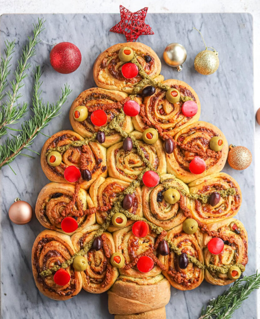 Pull-apart bread shaped like a Christmas tree with swirls of pesto and sun-dried tomato, decorated with olives.