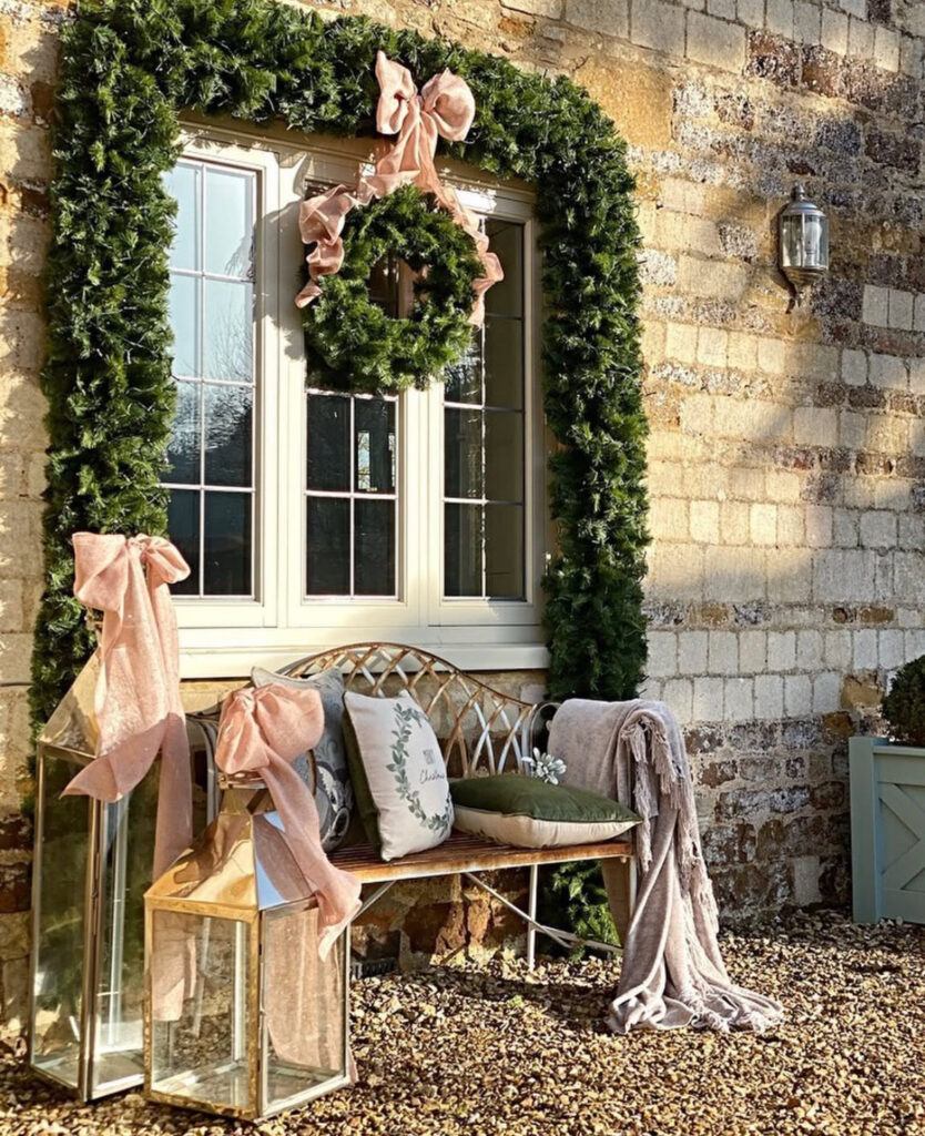 Cottage bench under window garland and wreath with blush bows and tall lanterns.