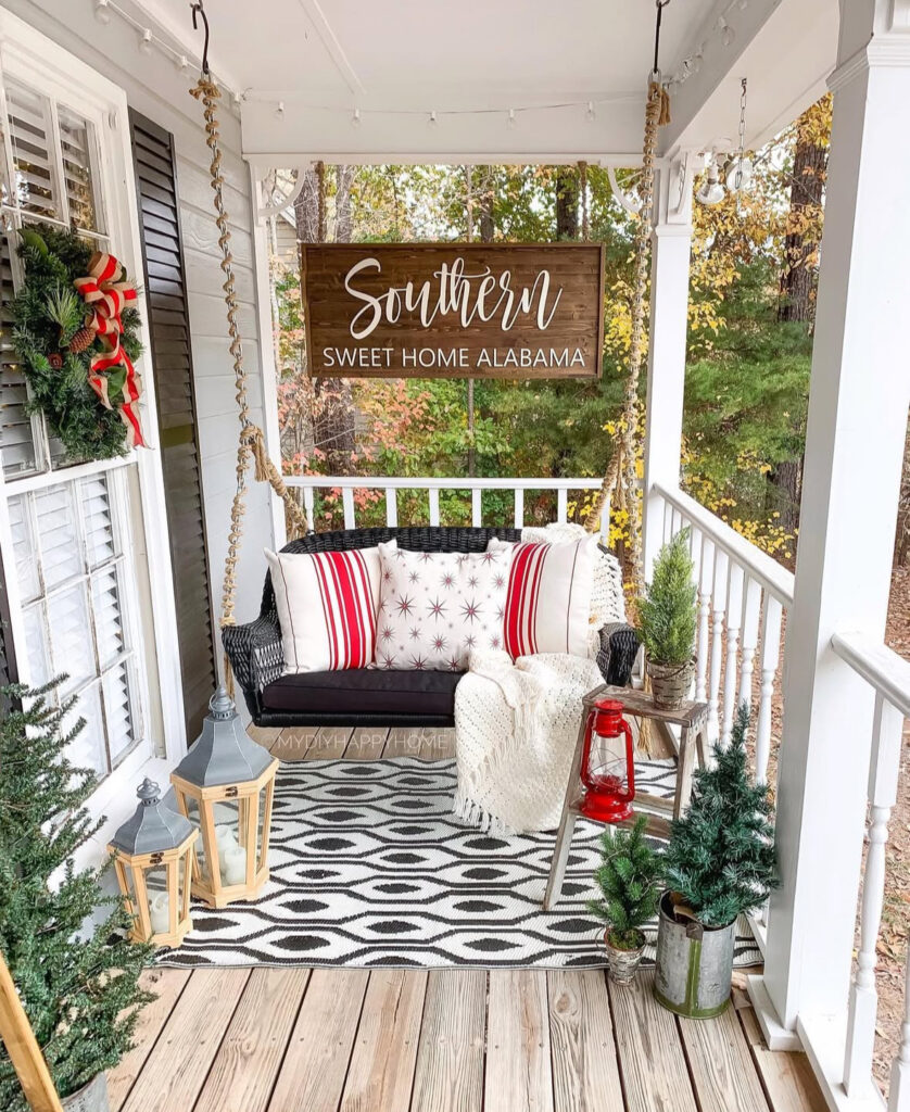 Southern porch swing with striped pillows, cozy throw, and small Christmas trees.