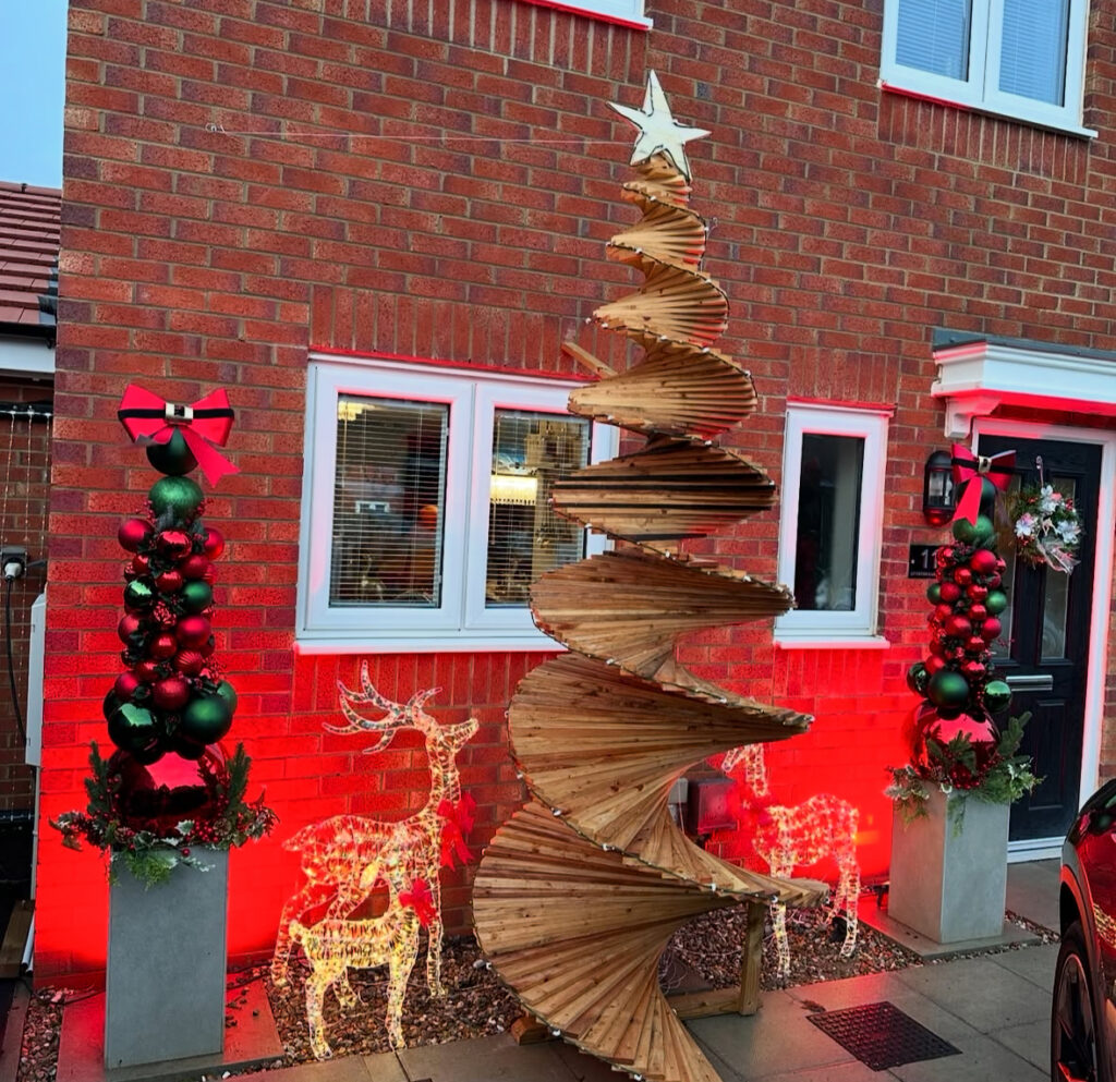 Modern yard featuring wooden spiral Christmas tree, lit reindeer, and ornament topiaries.