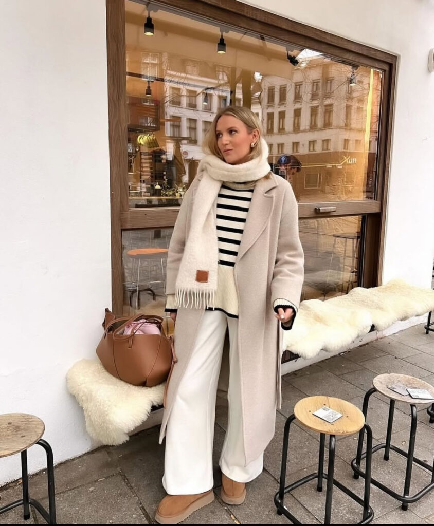 Breton striped sweater, ecru coat, oversized scarf, and wide white trousers at a café table.