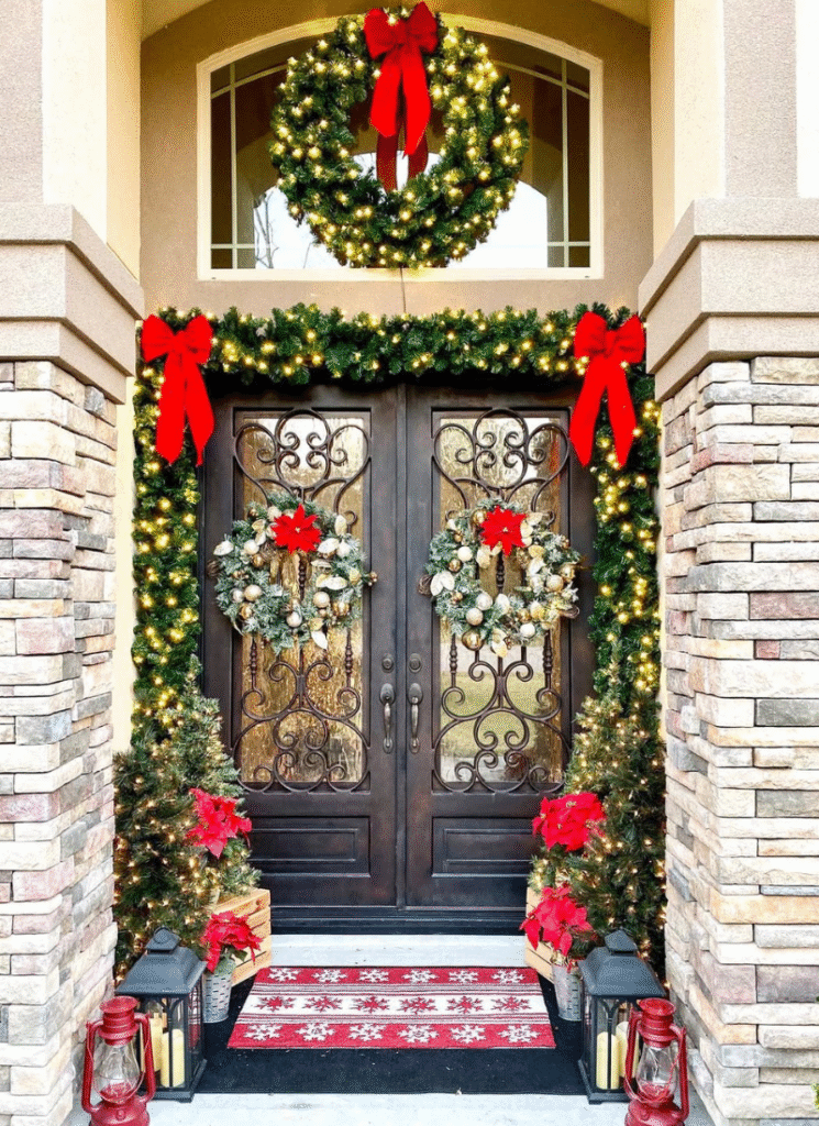 Grand double-door entry with twin wreaths, big bows, poinsettias, and lit evergreens.