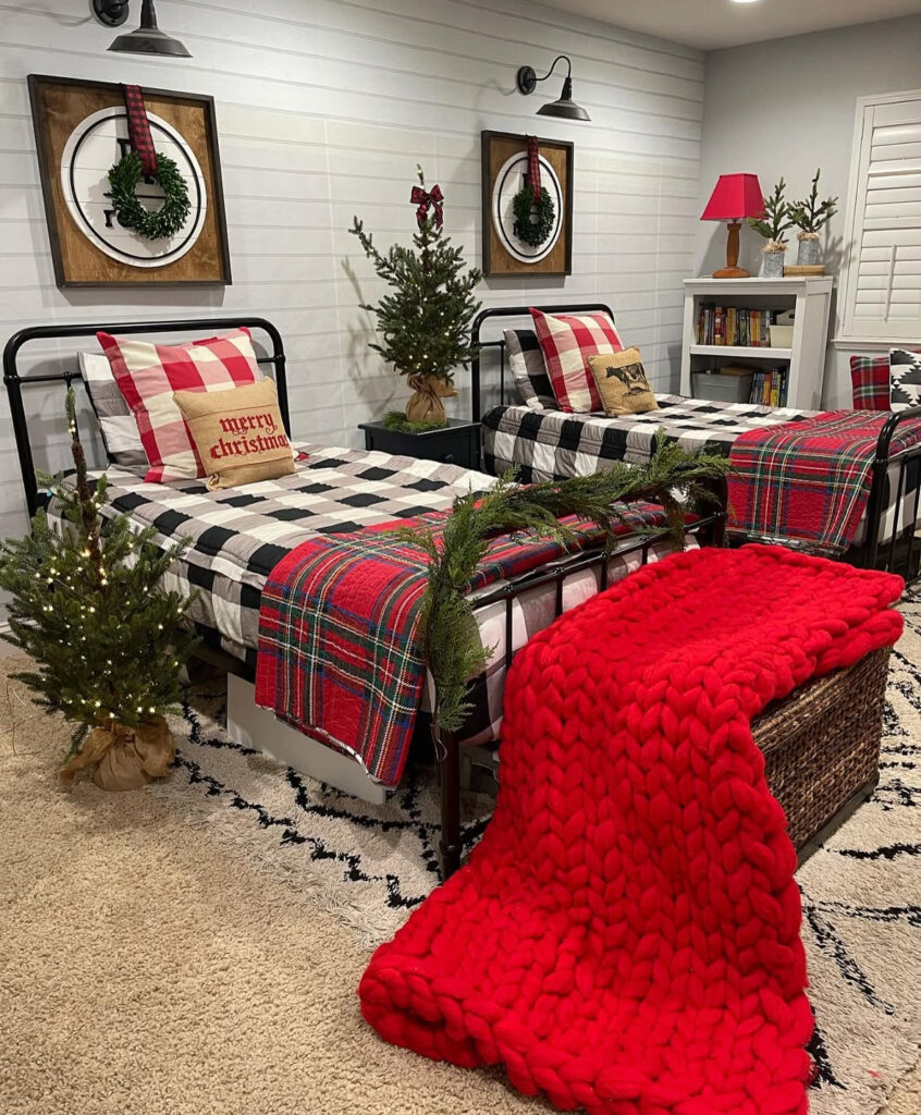 Twin metal beds with plaid throws and mini trees—camp-inspired kids Christmas bedroom ideas. Oversized red knit blanket steals the show.